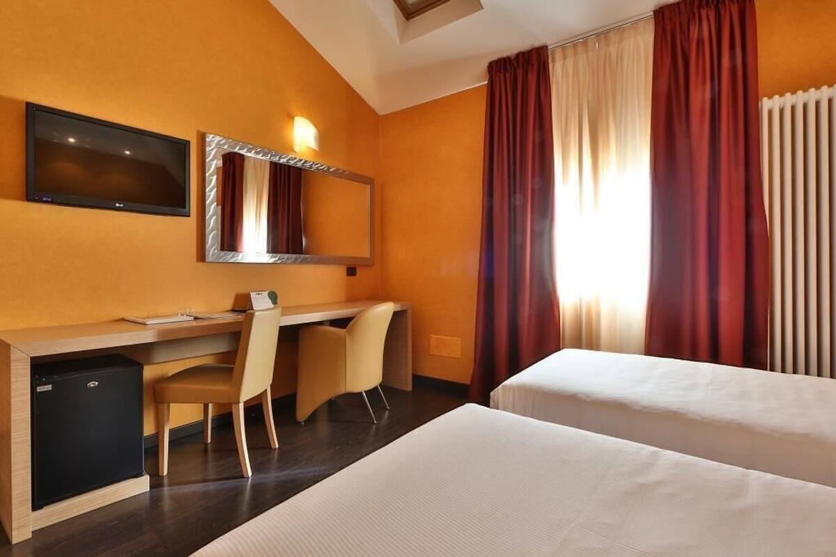 Una habitación de hotel con escritorio, dos camas, televisor y espejo.