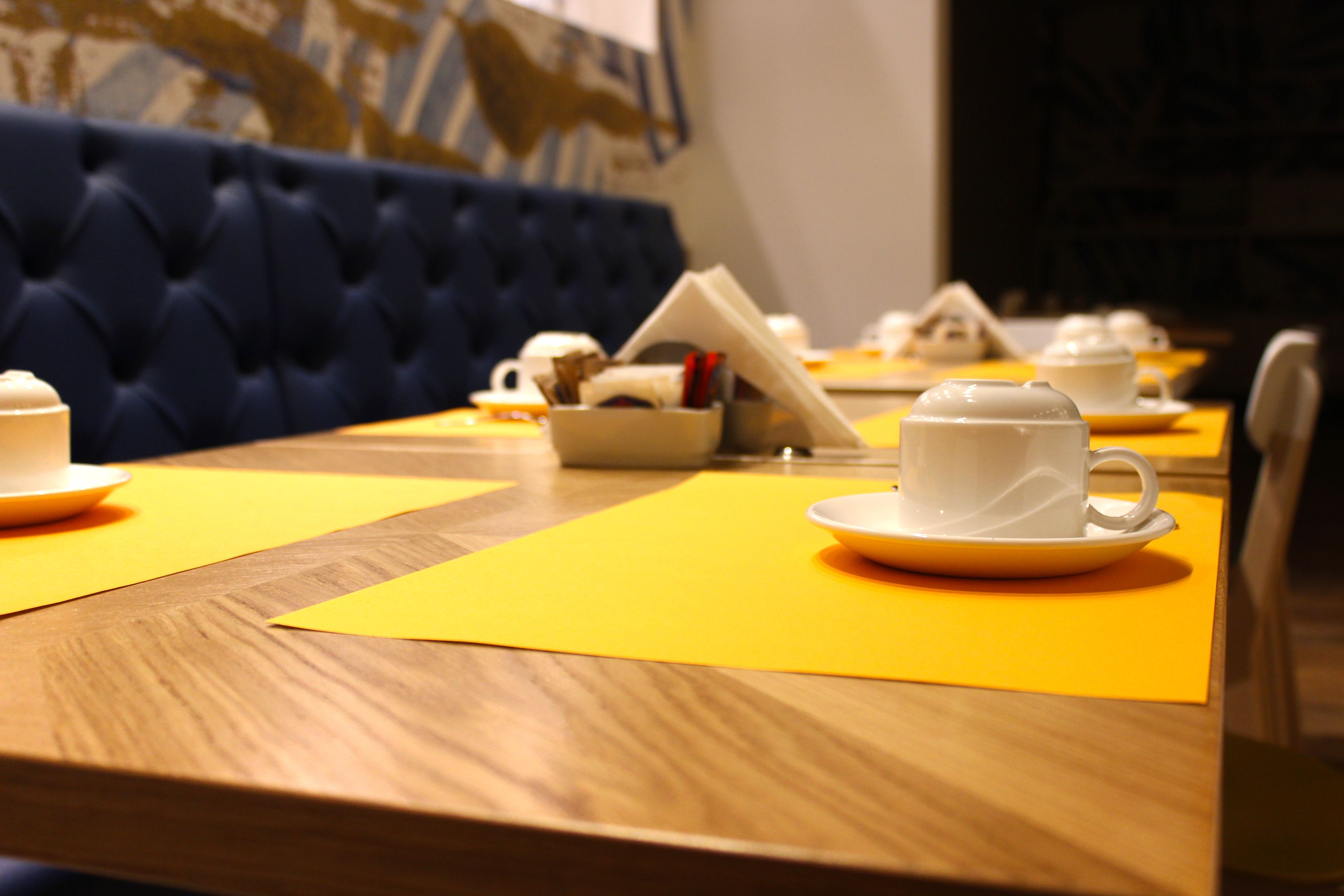A dining table with yellow placemats, white cups, and saucers.