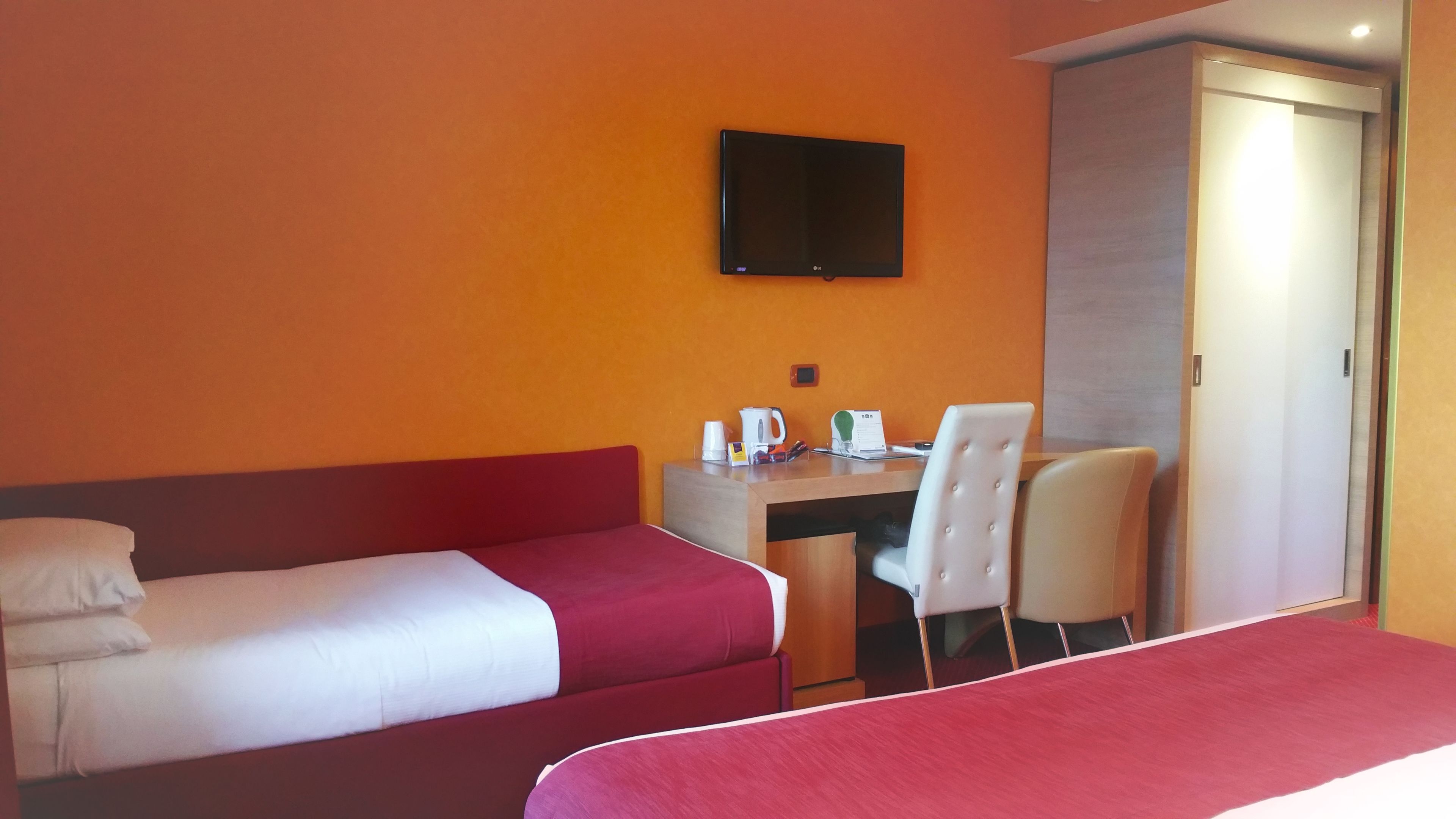 A hotel room with two beds, a desk, a chair, a television, and a wardrobe.