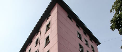 Un edificio de hotel rosa con un letrero que dice 'Hotel Piedmontese', un restaurante 'Saporpuro' y mesas al aire libre con sillas amarillas y blancas.