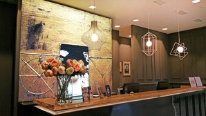 Un espace d’accueil avec un comptoir en bois, un vase de fleurs, un panneau d’affichage et un éclairage moderne suspendu au plafond.