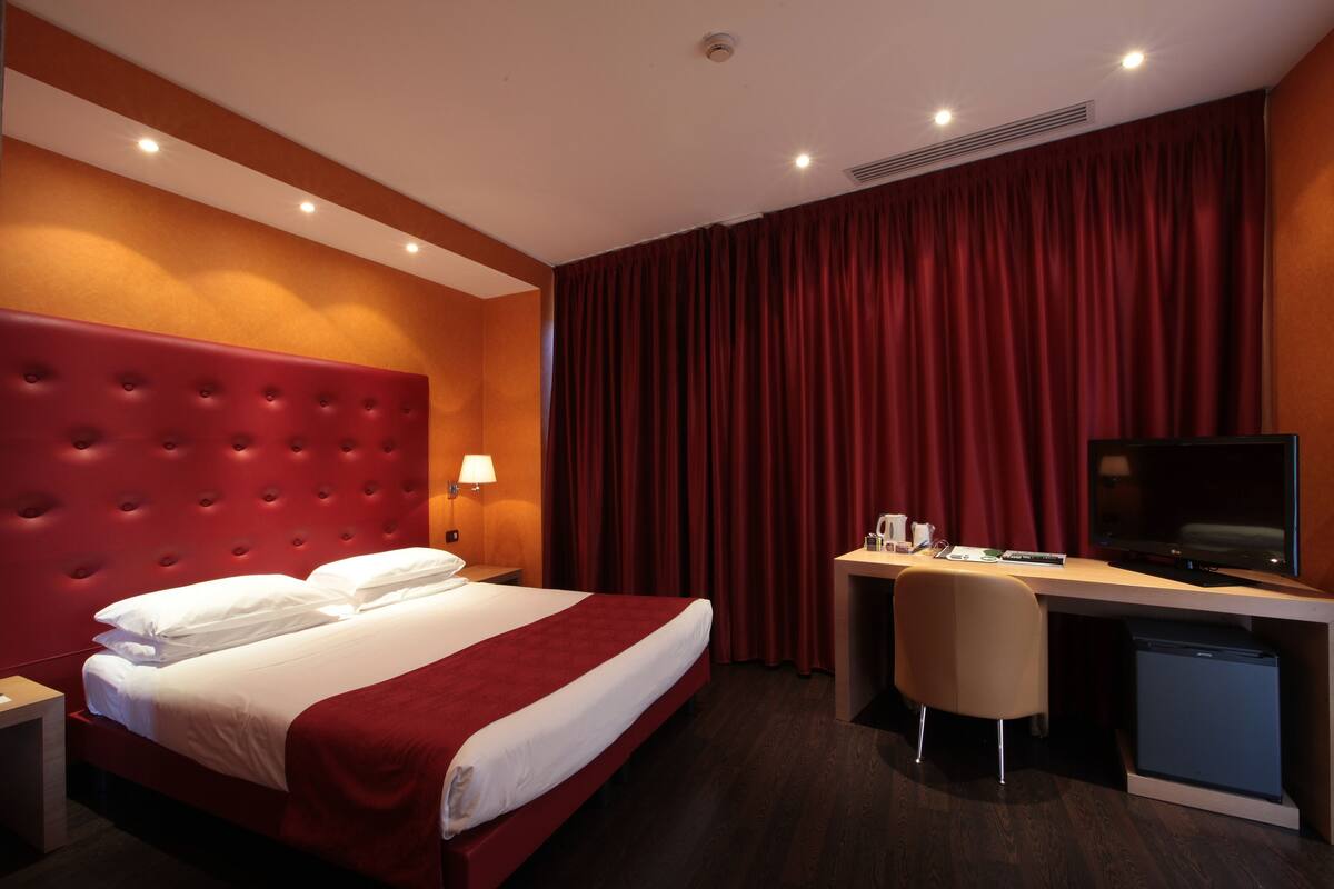 Una habitación de hotel con una cama grande, un escritorio con televisor y una silla.