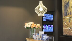 Un comptoir d’accueil agrémenté d’un luminaire suspendu moderne, d’un vase de fleurs et de plusieurs écrans diffusant des images de vidéosurveillance.