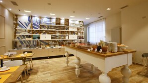 Un espace de repas moderne avec un îlot central, des tables et des chaises en bois. Un grand mur est décoré d’œuvres d’art et des étagères sont remplies de divers objets.
