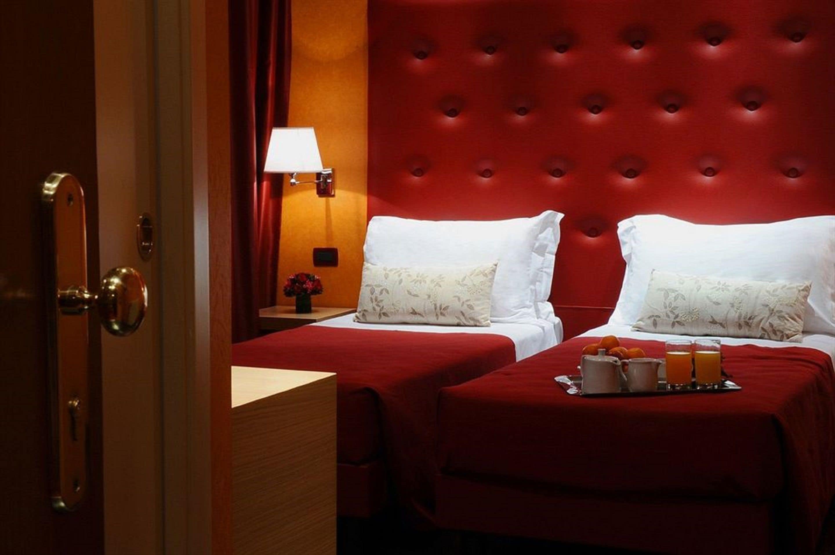 A hotel room with two beds, red headboard, and a tray with breakfast items.