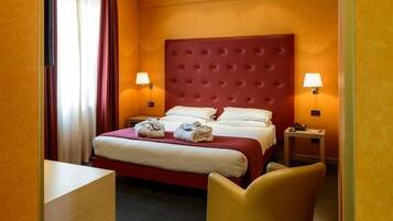 Camera d'albergo con un grande letto, due lampade ai comodini, una sedia e una scrivania.