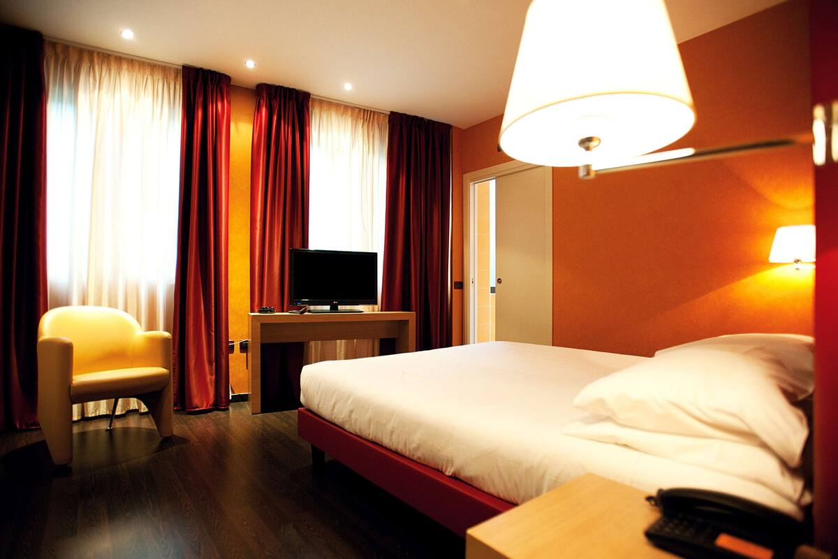 Una habitación de hotel con cama, escritorio, televisión, silla y lámpara.