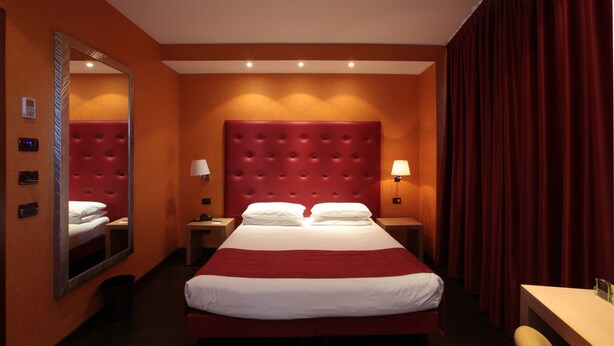 Une chambre d’hôtel avec un grand lit, un miroir, deux tables de chevet avec des lampes, un bureau et un rideau rouge.