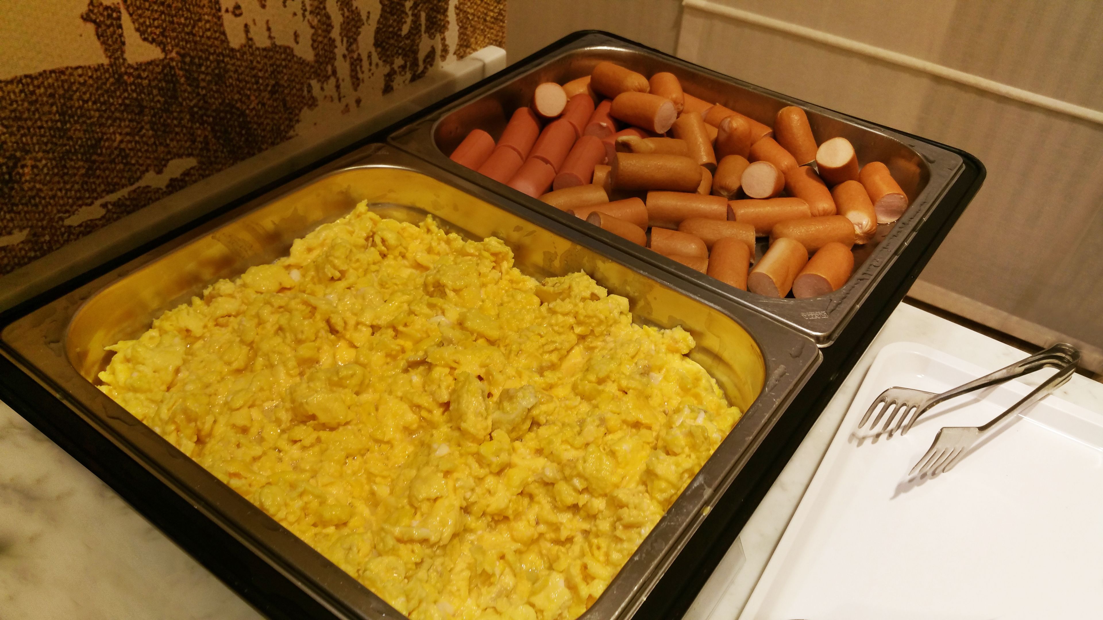 A buffet with scrambled eggs and hot dogs.