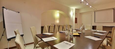 A conference room with a long table, chairs, a whiteboard, and a projector screen.