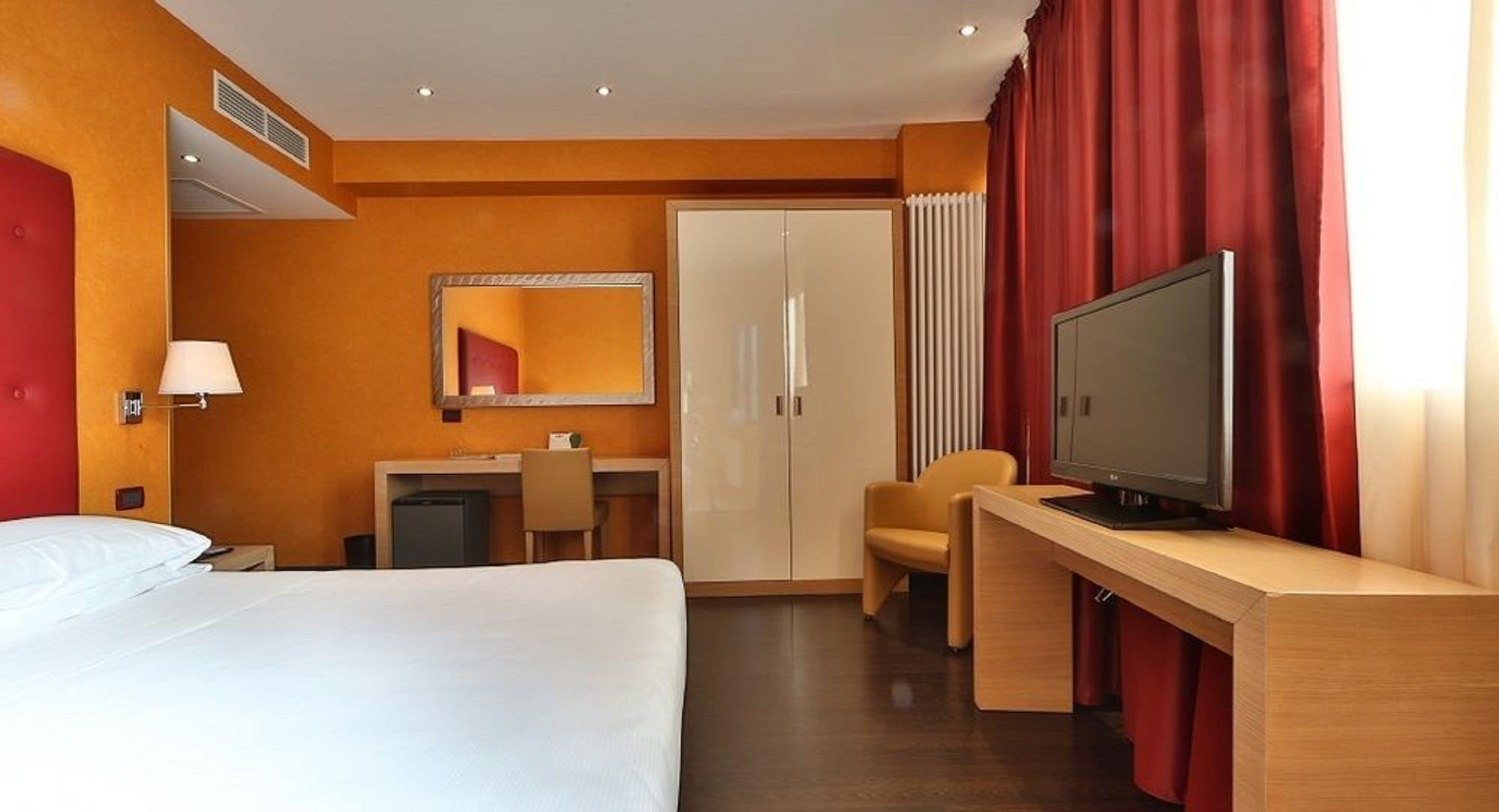 Une chambre d’hôtel comprenant un lit, un bureau avec une télévision, un miroir, une armoire et une chaise.