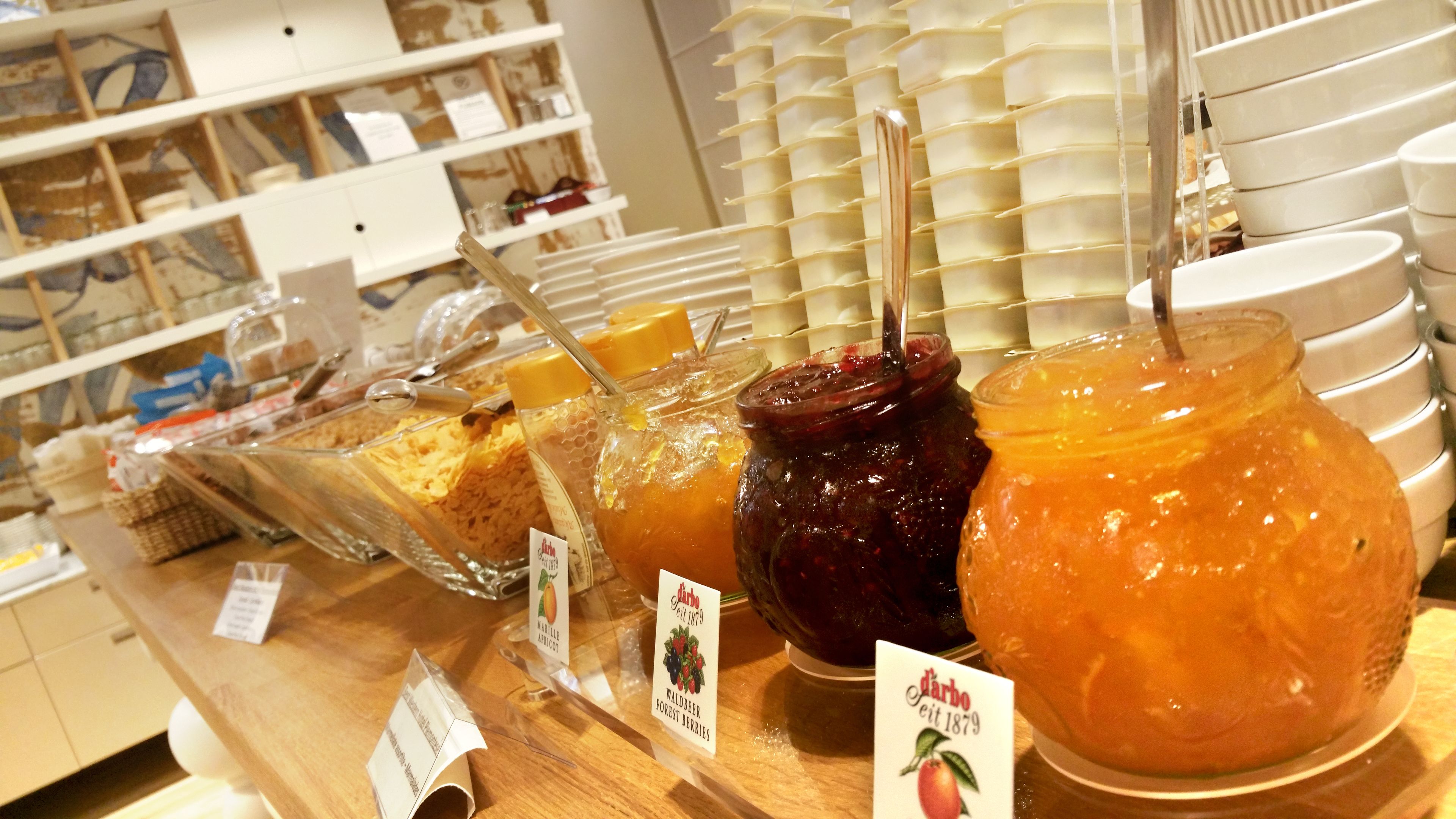 Forskellige marmelader og syltetøjsvarianter i glas med etiketter, udstillet på en trædisk i en butik.