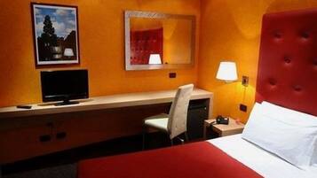 A hotel room with a bed, a desk with a chair, a television, a mirror, and a lamp.