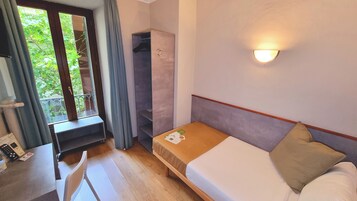 Una camera d'albergo compatta con un letto singolo, una scrivania e un armadio.