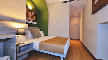 Una camera d'albergo piccola e stretta con un letto, un comodino, una lampada e una parete verde decorativa.