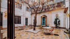 Un patio con suelo de baldosas, un árbol en el centro y mobiliario exterior.