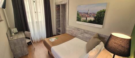 A hotel room with a bed, a desk, a chair, a lamp, and a cityscape view.