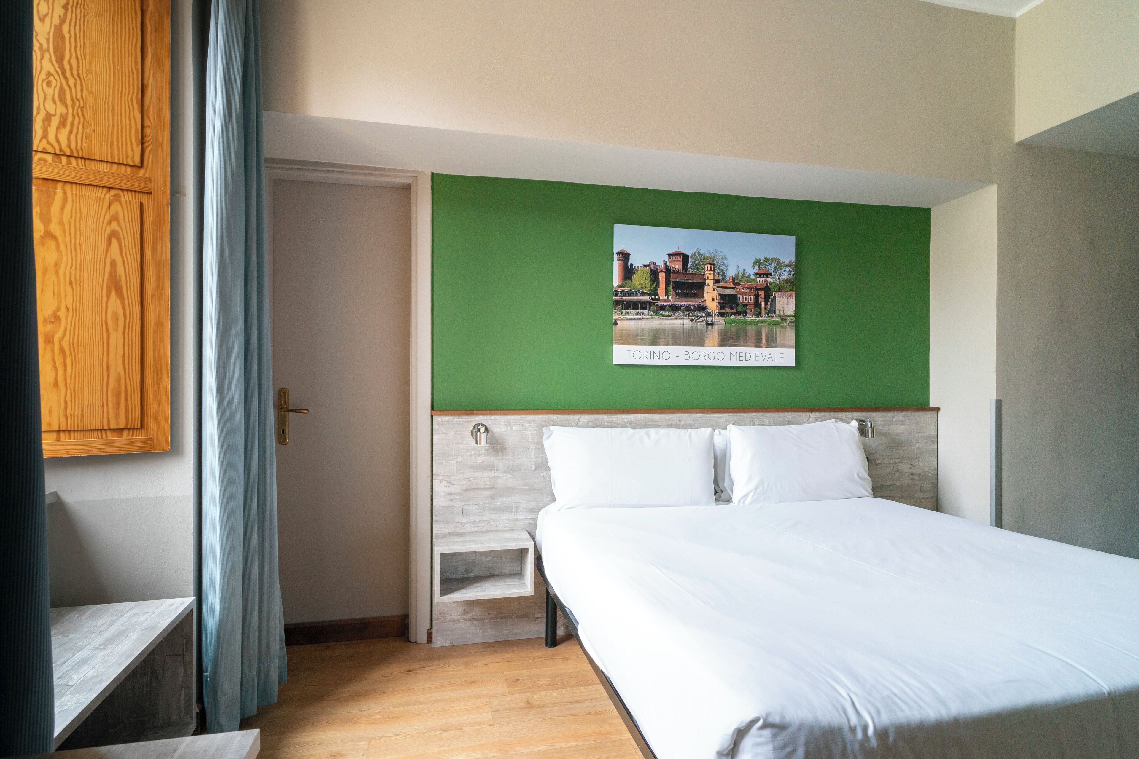 A hotel room with a bed, a green wall, and a framed picture of a cityscape.