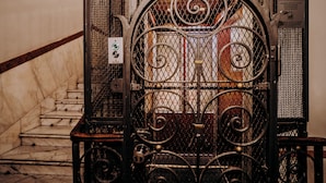 Una reja metálica con diseños intrincados, una escalera de mármol y un cartel con instrucciones de seguridad.