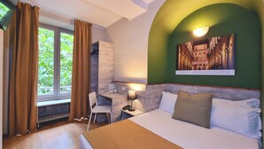 Habitación de hotel con cama, escritorio, silla, lámpara y un cuadro en la pared.