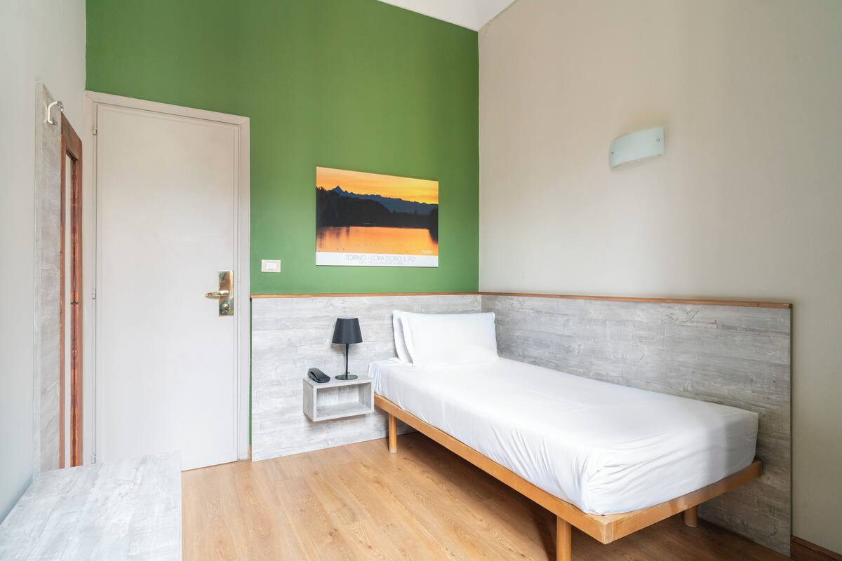 Un dormitorio con una cama de madera, una mesita de noche con una lámpara, una pared verde y un cuadro con una imagen de atardecer.