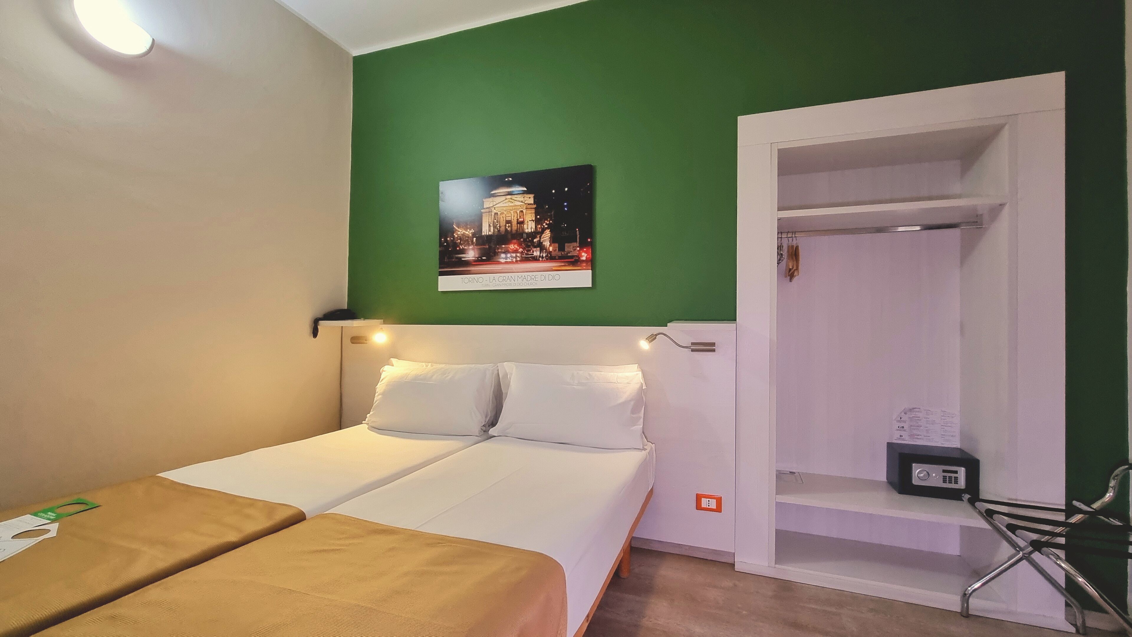 A hotel room with a bed, a small table, a chair, a wardrobe, and a poster on the wall.