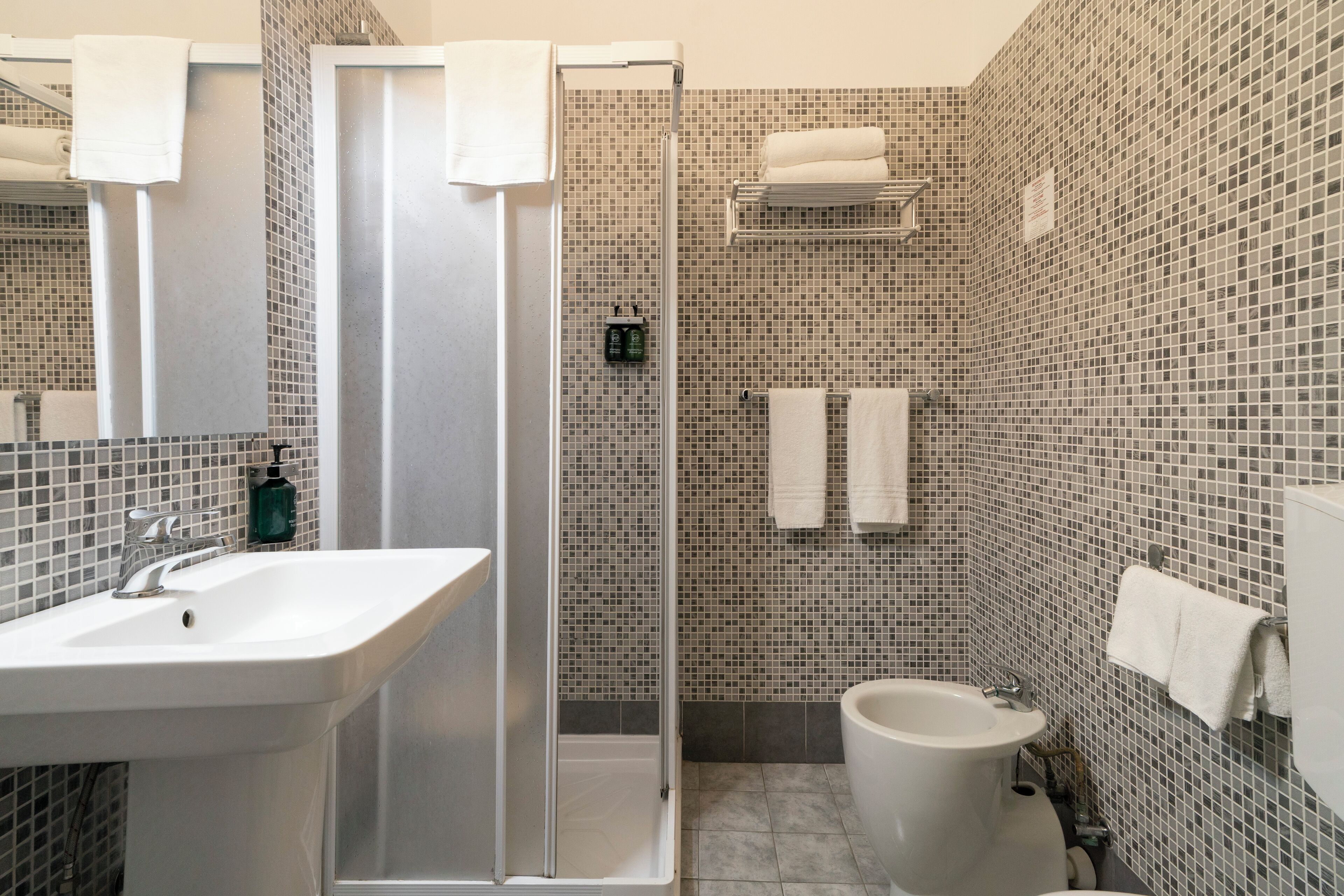 A bathroom with a shower, sink, bidet, and tiled walls.