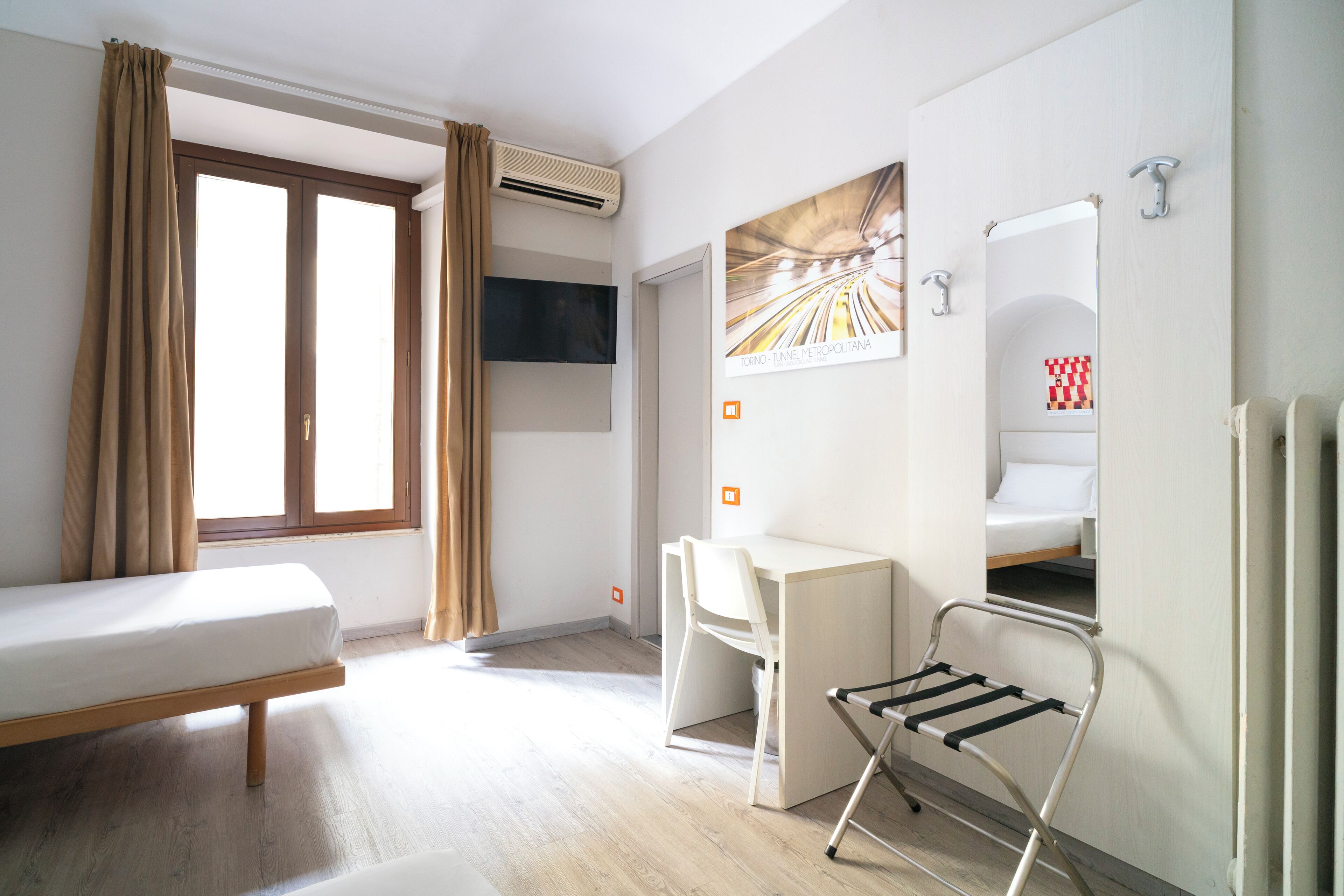 Una camera d'albergo con un letto, una scrivania, una sedia, una televisione e uno specchio.
