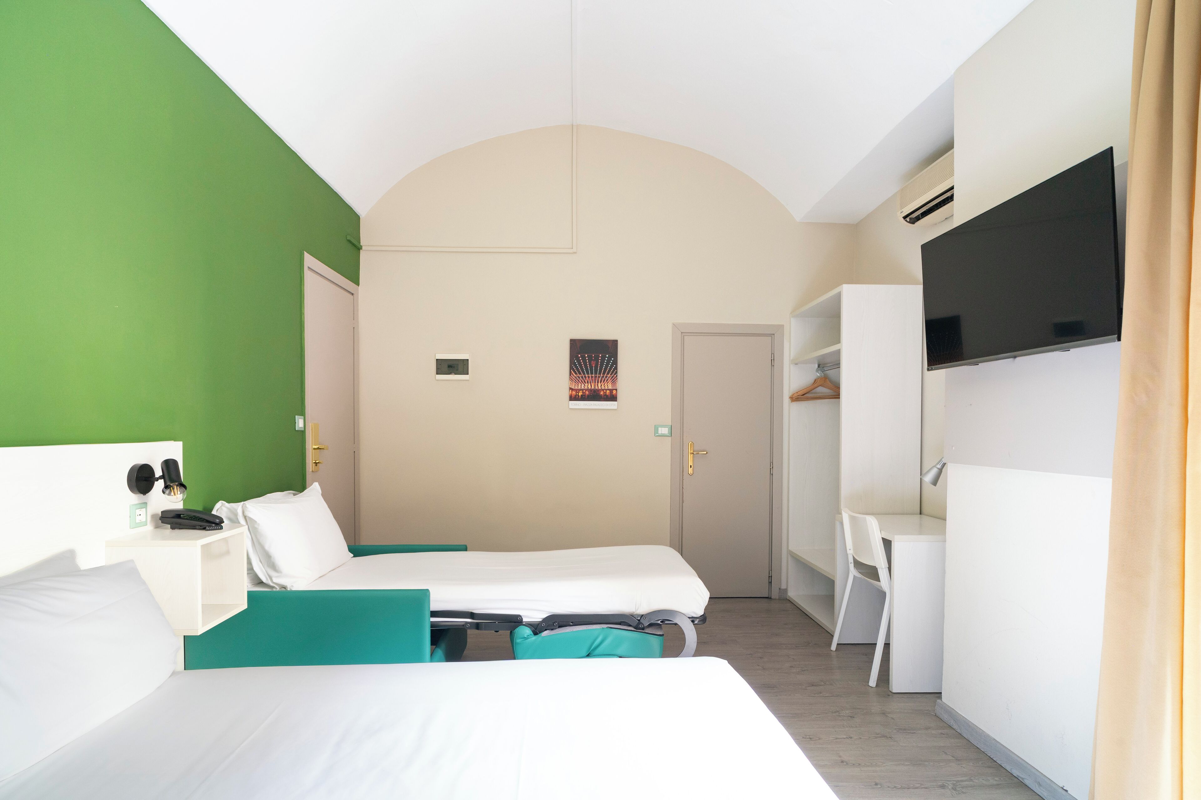 A hotel room with two beds, a desk, a TV, and a wardrobe.