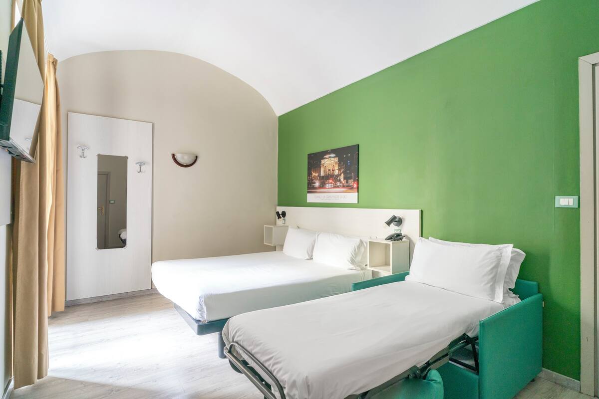Habitación de hotel con dos camas, una pared de acento verde, un cuadro enmarcado y una puerta blanca.