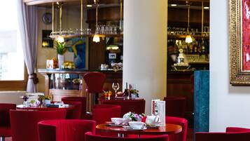 Un restaurante con sillas y mesas rojas, una zona de bar al fondo y un cuadro en la pared.