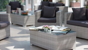 A modern outdoor seating area with wicker furniture and cushions, featuring a glass coffee table with a book and flowers. - Hotel Terme Millepini (Montegrotto Terme)