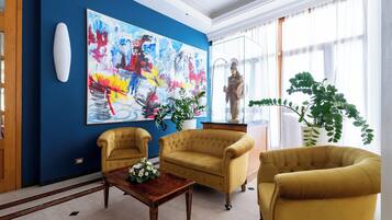 A room with a blue accent wall, a large abstract painting, two yellow armchairs, a wooden coffee table, and a statue.