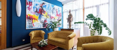 Een kamer met een blauwe accentmuur, een groot abstract schilderij, twee gele fauteuils, een houten bijzettafeltje en een beeld.