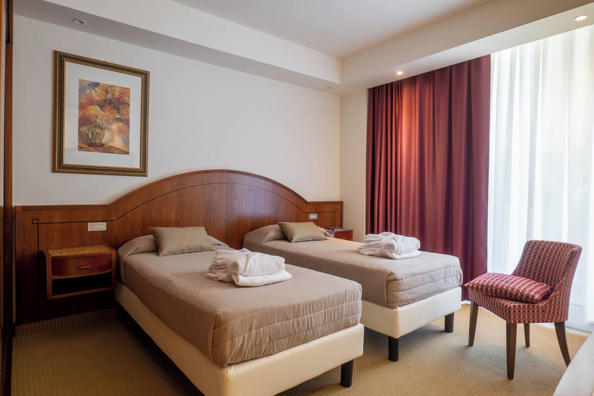 A hotel room with two beds, a wooden headboard, a red chair, and a painting on the wall.