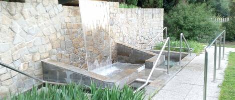 A stone water feature with a cascading waterfall, metal steps, and a metal railing.