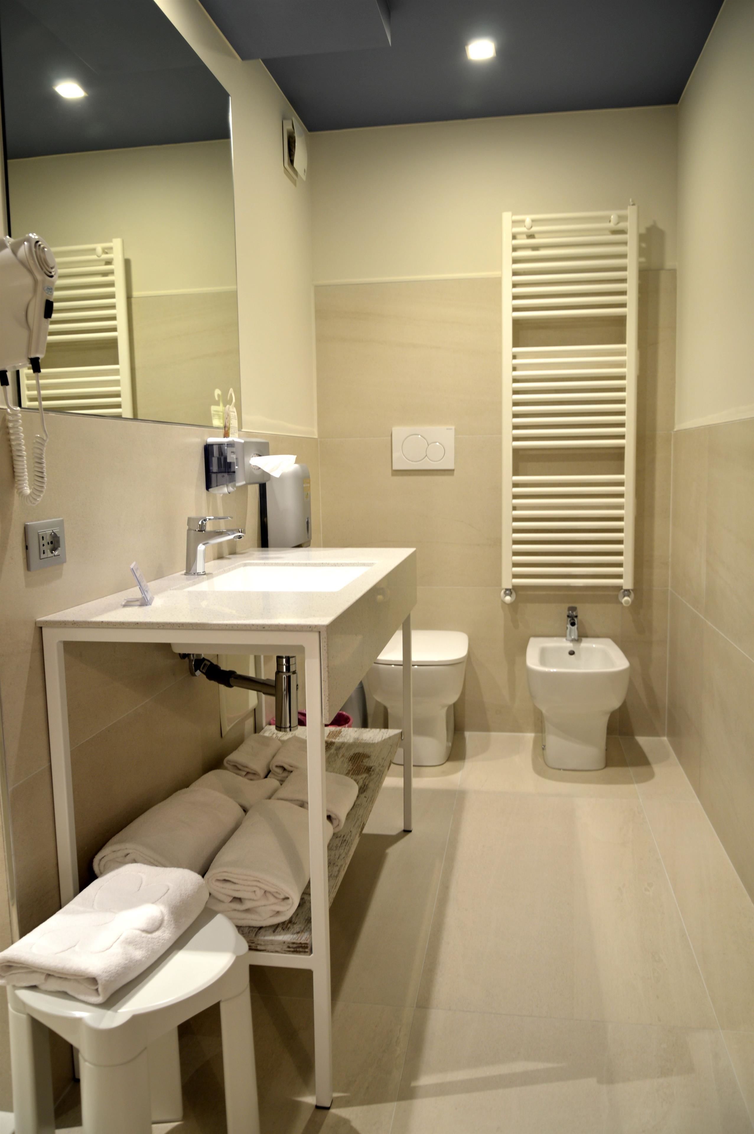 A modern bathroom with a white vanity, a toilet, a bidet, and a towel rack.