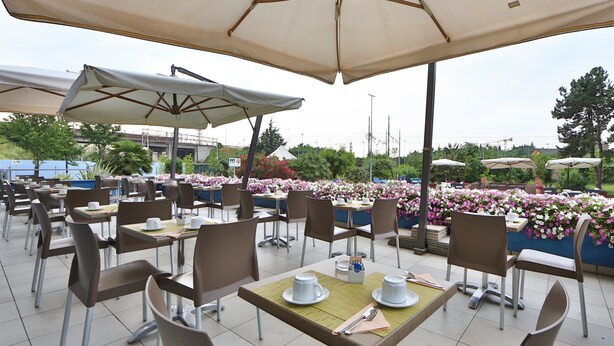 Un café en plein air avec des tables, des chaises, des parasols et des jardinières fleuries.