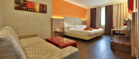A hotel room with a bed, a sofa, a desk, and a painting on the wall.