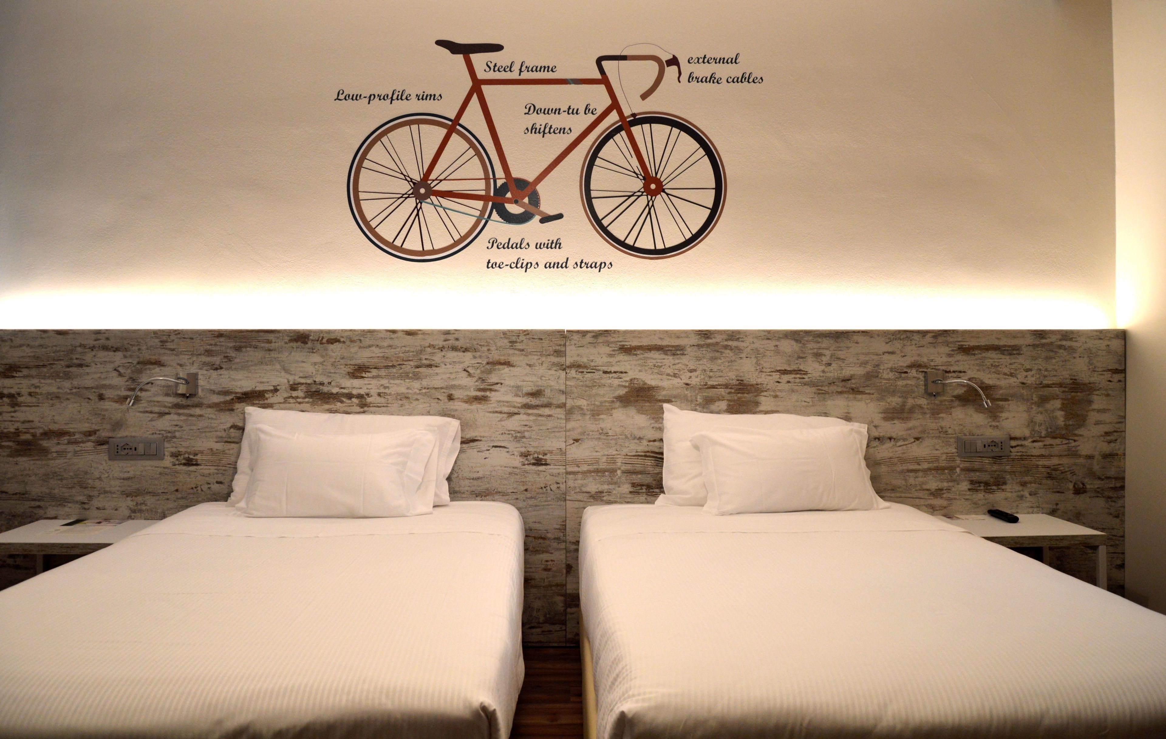 A hotel room with two beds, a wooden textured wall, and a wall-mounted bicycle illustration.