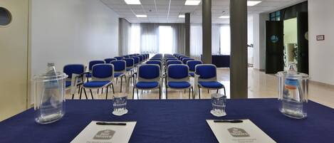 Uma sala de conferências com fileiras de cadeiras azuis, uma mesa com garrafas de água e uma placa da Best Western.