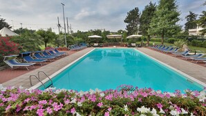 Une piscine entourée de verdure et de fleurs, avec des chaises longues et des parasols.