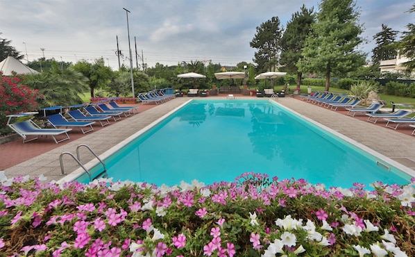Una piscina con tumbonas y sombrillas, rodeada de follaje y flores.