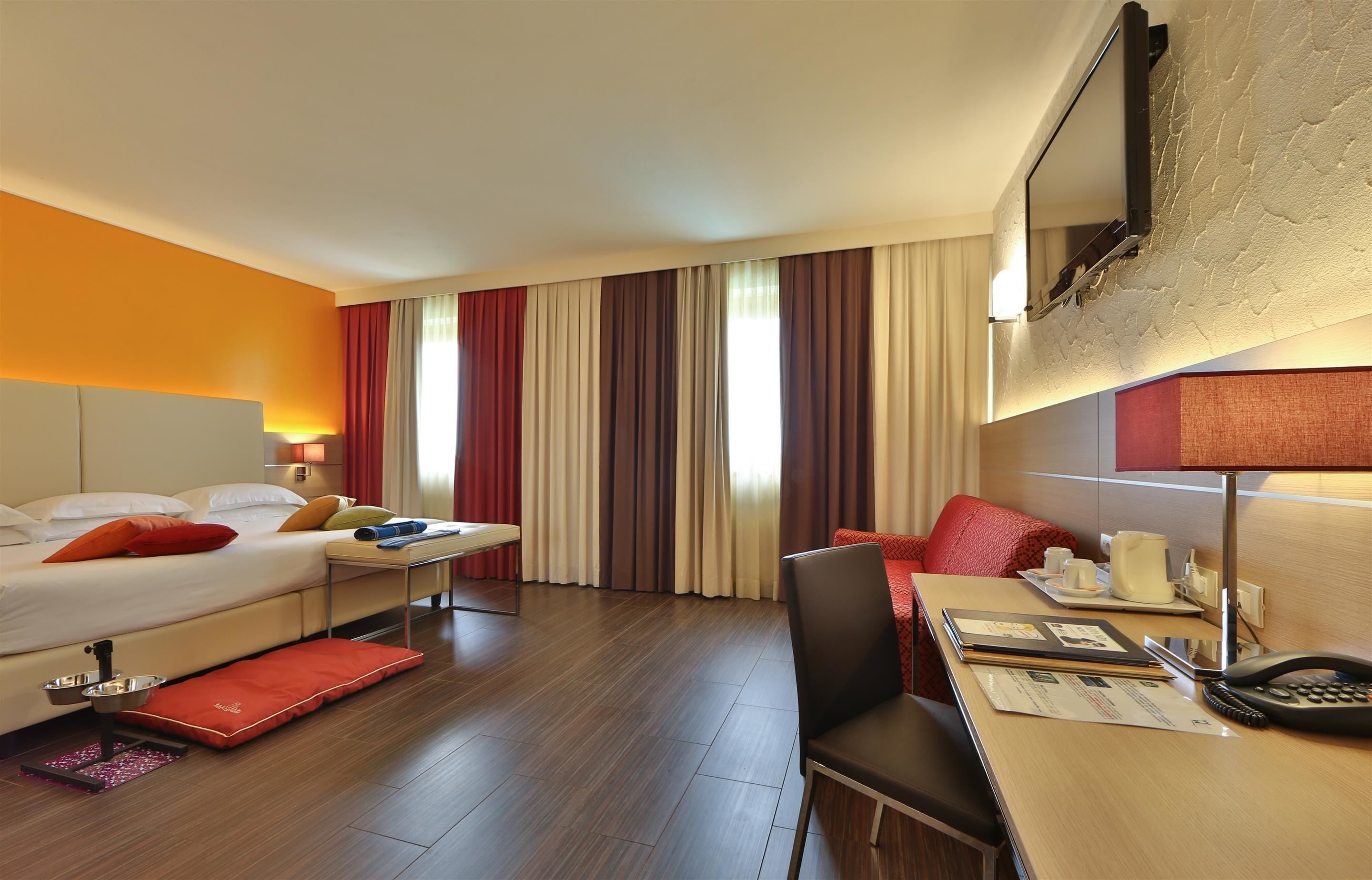 Una habitación de hotel con cama, escritorio, silla y televisión instalada en la pared.