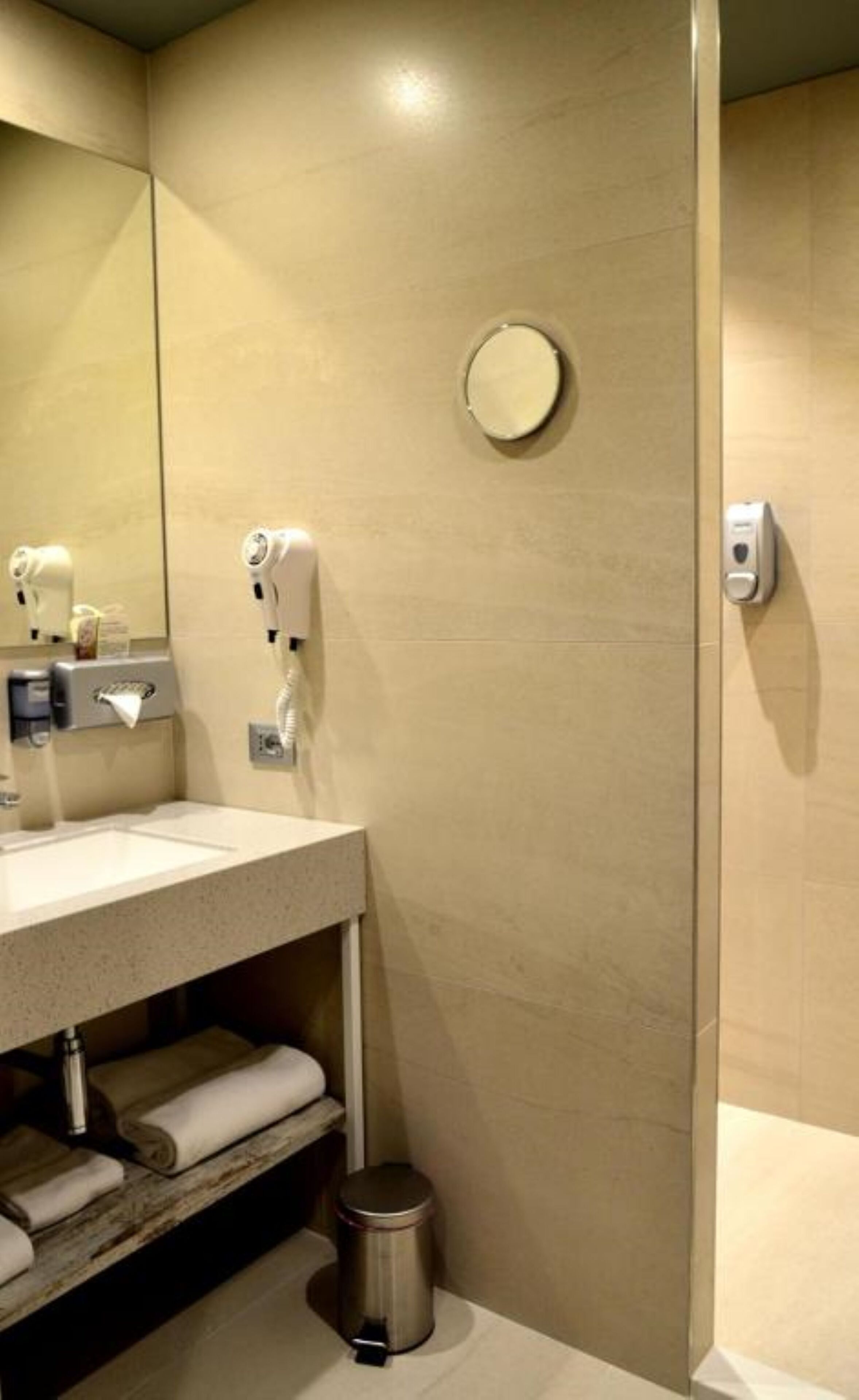 Un bagno moderno con lavandino, specchio, erogatore di asciugamani e cestino.