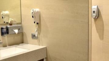 Un bagno moderno con lavandino, specchio, erogatore di asciugamani e cestino.
