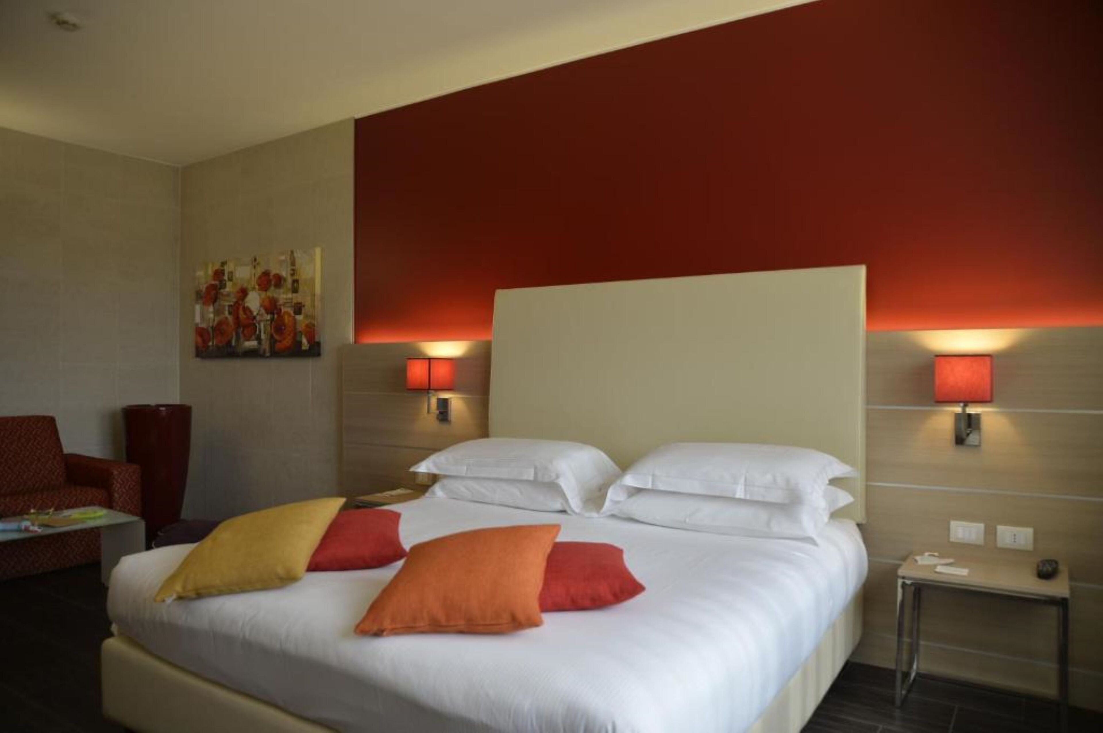 Habitación de hotel con una cama grande, dos lámparas de noche, una pared de acento roja y un cuadro en la pared.