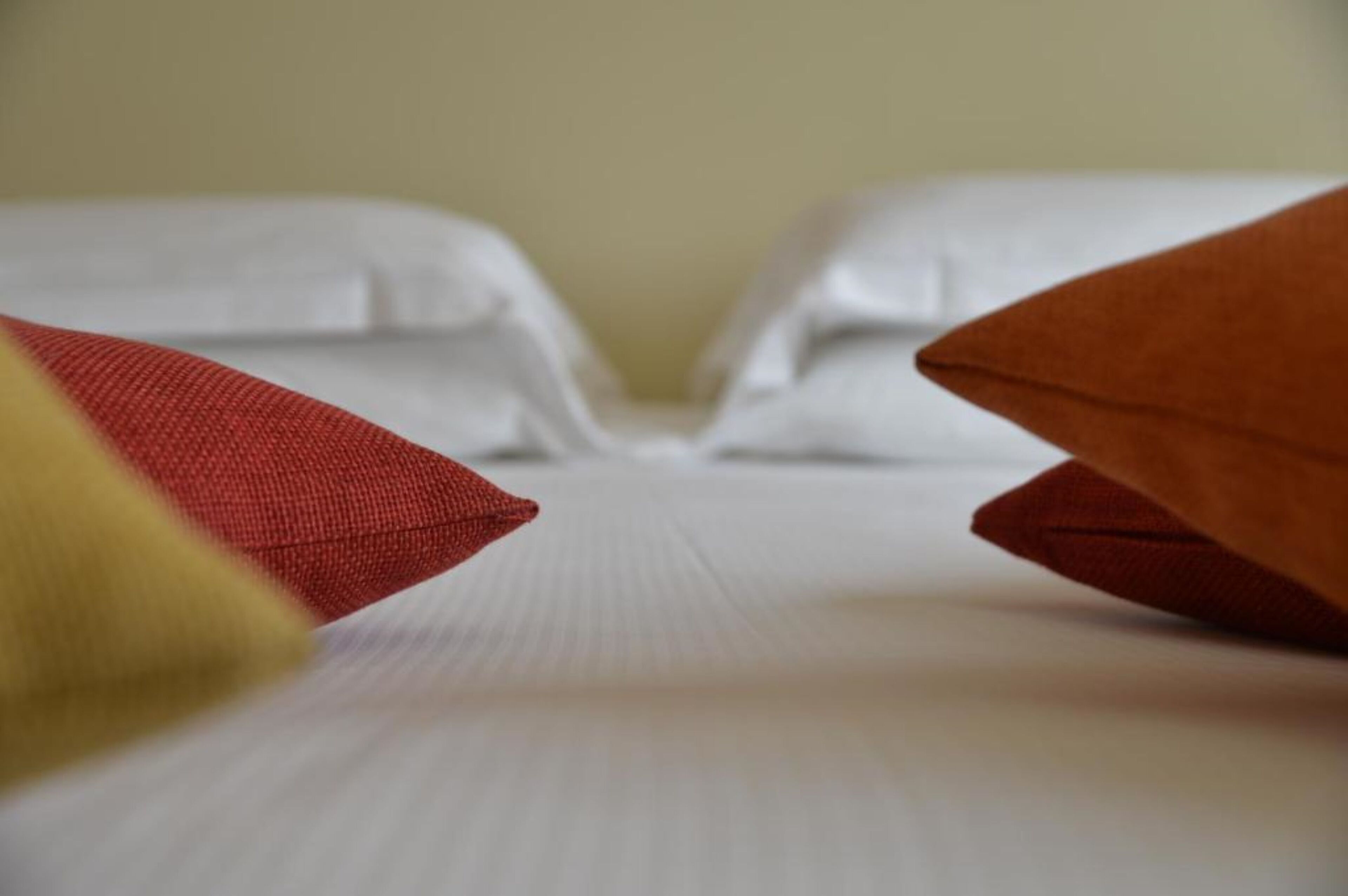 Un letto rifatto con lenzuola bianche e due cuscini, uno rosso e uno giallo.