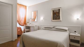 A bedroom with a bed, bedside tables, a nightstand, a desk, and a chair.