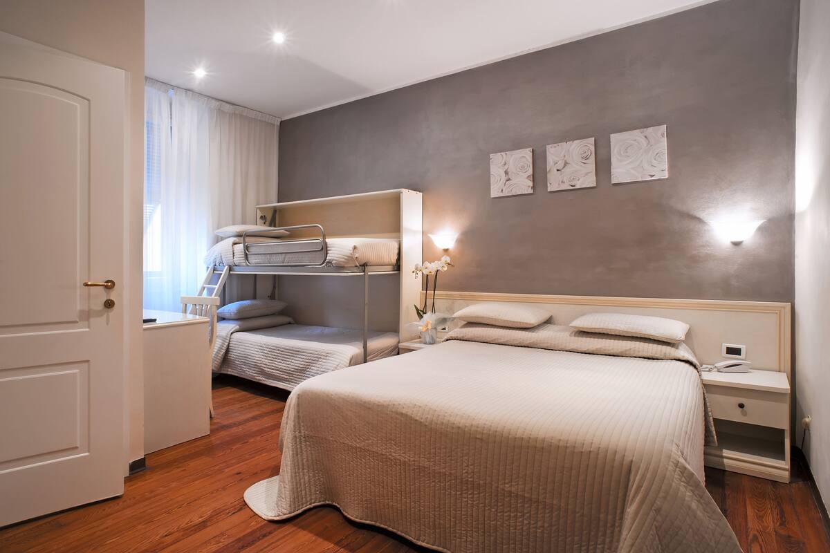 A bedroom with a bunk bed, a single bed, a bedside table with a lamp, and a nightstand with a phone.